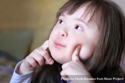 Portrait of a girl with Down syndrome with her fingers on her cheeks 4BRpX4