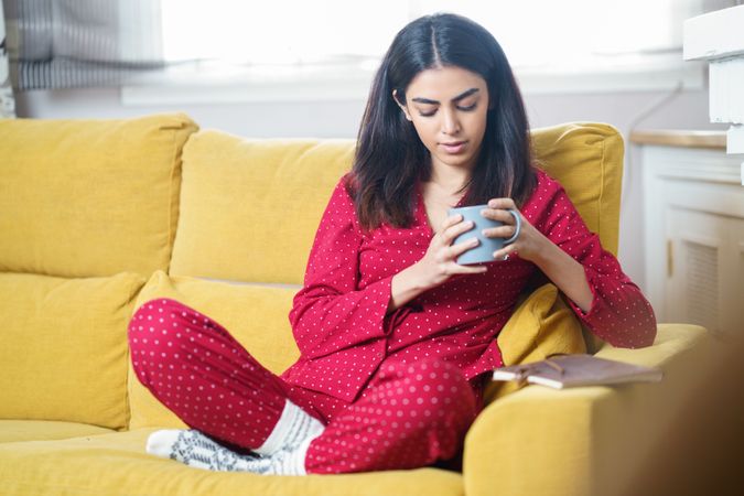 Woman sipping tea on yellow sofa at home