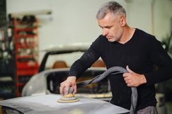 Mechanic grinding paint from car detail