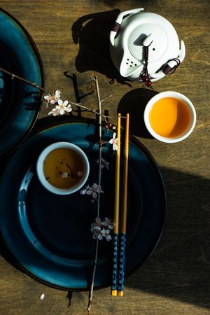 Top view of table setting with chop sticks on ceramic navy plate and decorative cherry blossom branch and tea pot