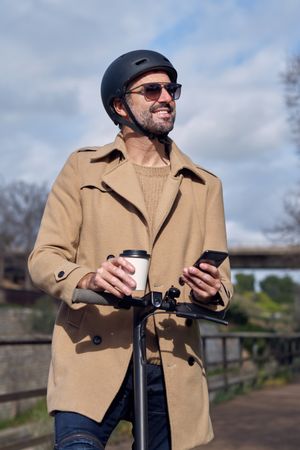 Man with coffee and smartphone on scooter