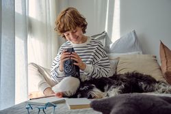 Smiling schoolboy with aged photo camera and dog on bed