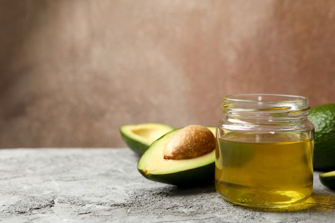 Ripe fresh avocado and oil on gray table, close up