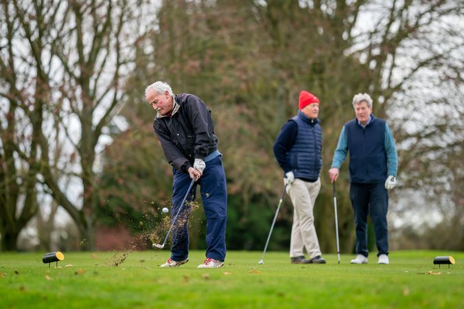 Man swinging on golf course with friends