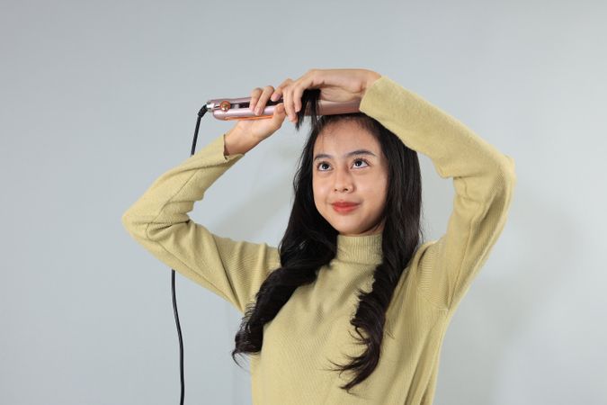 Young Asian Teenager using Hair Straightener for Her Bangs