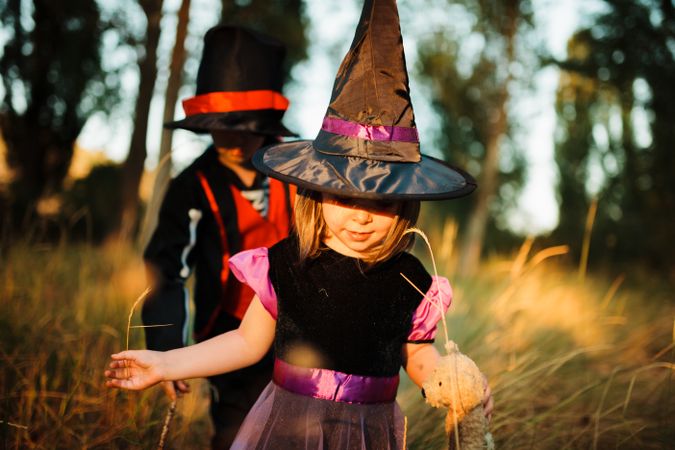 Little girl in witch costume walking with her brother in the long grass