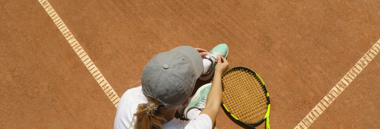Woman ties shoelace on clay court with racket
