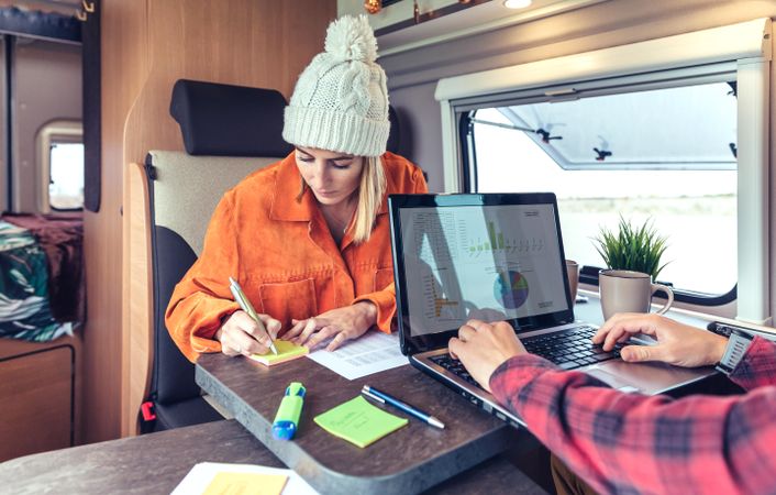Male and female friends working remotely in back of van while camping