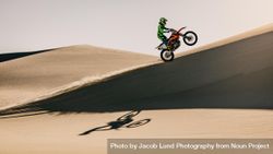 Side view of motocross bike rider riding up over sand dunes bYQDXb