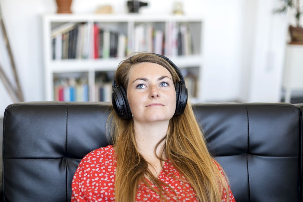 Blonde young woman listening to music on headphones while relaxing on sofa