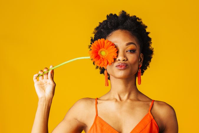 Black woman holding a flower over her eye