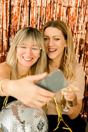 Cheerful girlfriends taking selfie in evening dress on party