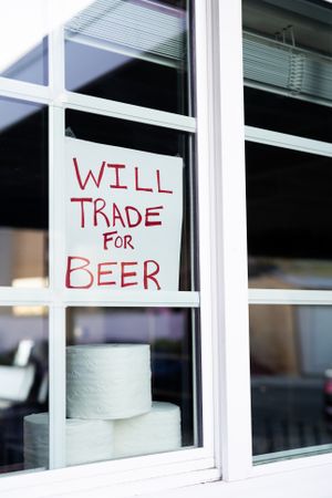 Handmade sign hanging in house window offering to trade toilet paper for alcohol