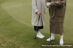 Two people in coats holding golf clubs 4N3Veb