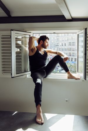 Young happy man sitting on window