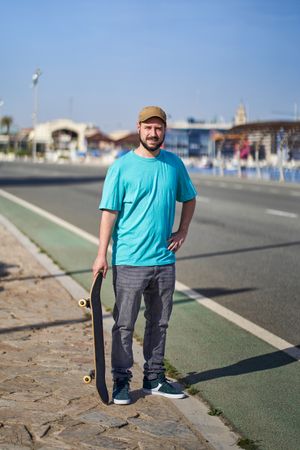portrait of a young man with skateboard on a road next to the harbor in the morning