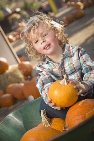 Little Boy Sitting and Holding His Pumpkin at Pumpkin Patch.