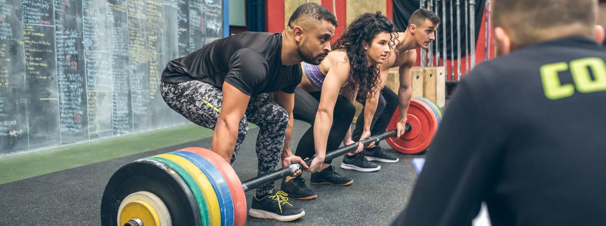 Multiracial team lifting weights in the gym with their coach