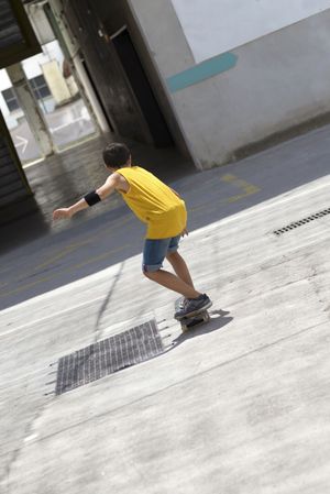 Back view of a male skateboarder in yellow riding on a sunny day