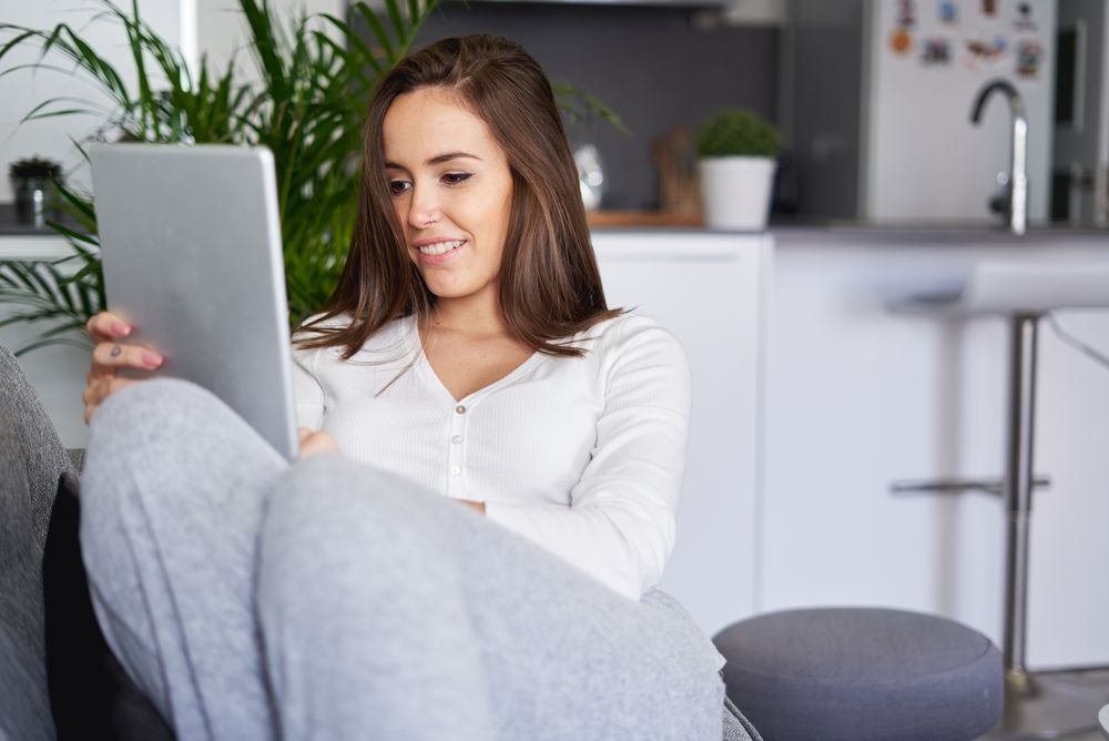 Smiling woman browsing on tablet and sitting on settee
