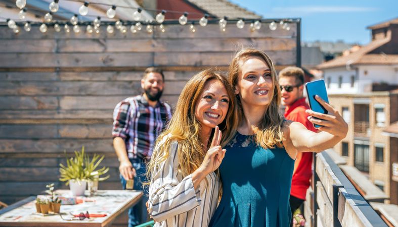 Two female friends taking a selfie in rooftop on a summer party