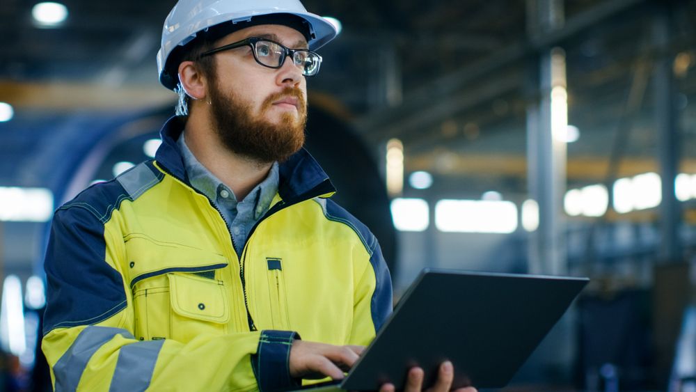 Industrial Engineer in Hard Hat Wearing Safety Jacket Uses Laptop.
