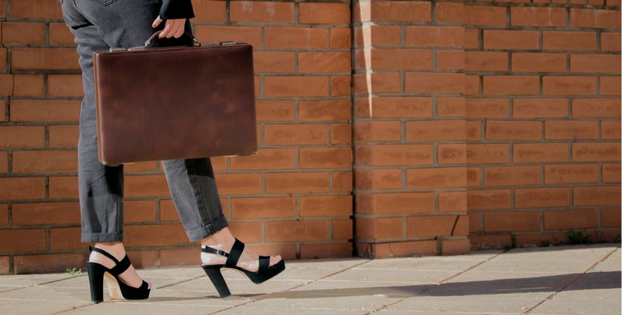 Woman wearing heels and suit holding briefcase walking on sidewalk