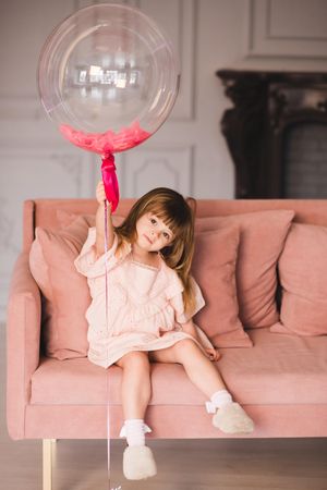 Young girl holding a balloon sitting on pink sofa