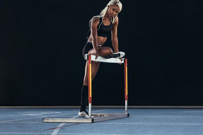 Fit woman leaning on hurdle on athletic track