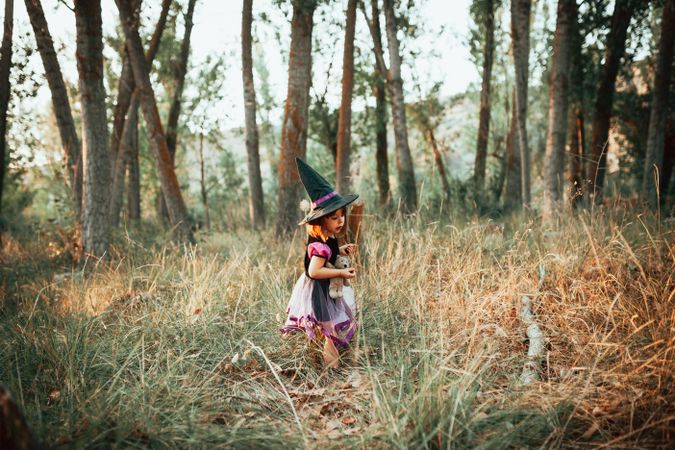 Girl in the forest in witch costume with her teddy bear