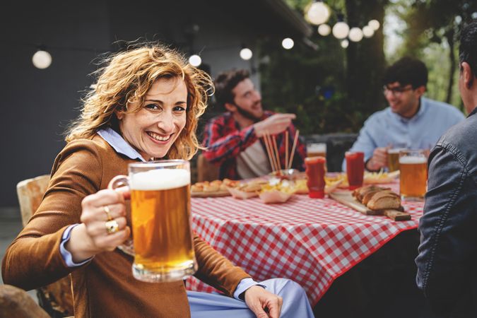 Portrait of  woman looking at camera and holding glass with lager beer while sitting at the farmhouse table
