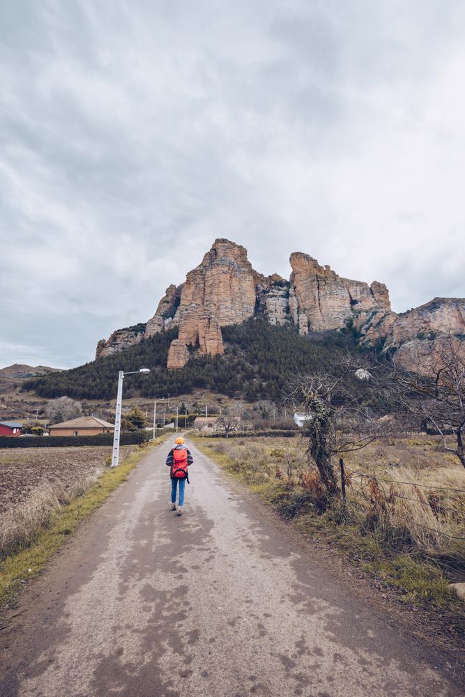 Hiker with backpack walking along rural road to cliff on gloomy day