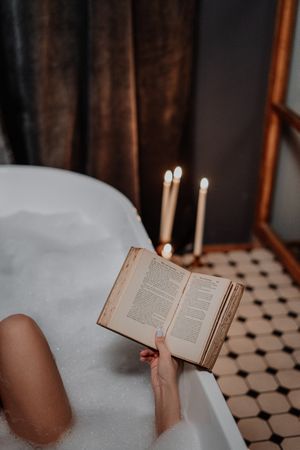 Cropped image of woman reading a book in the bathtub