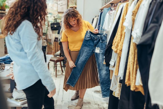 Fashion store owner showing jeans to female customer