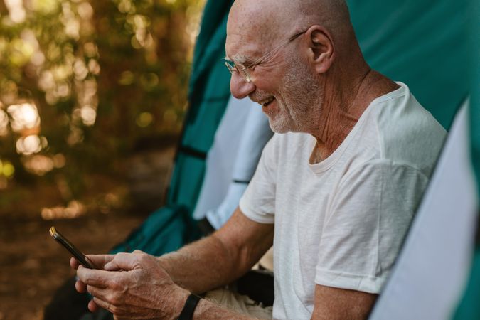 Smiling mature man sitting in tent using his mobile phone