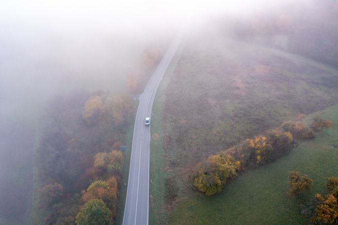 Drone aerial image with a winding road crossing an autumn forest on a foggy morning