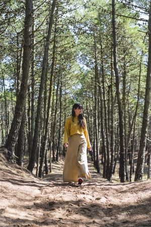 Adult woman walking over a path under the trees in the forest. Vertical shot.