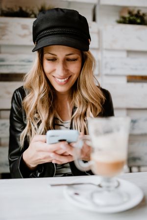 Smiling curly woman browsing smartphone at table
