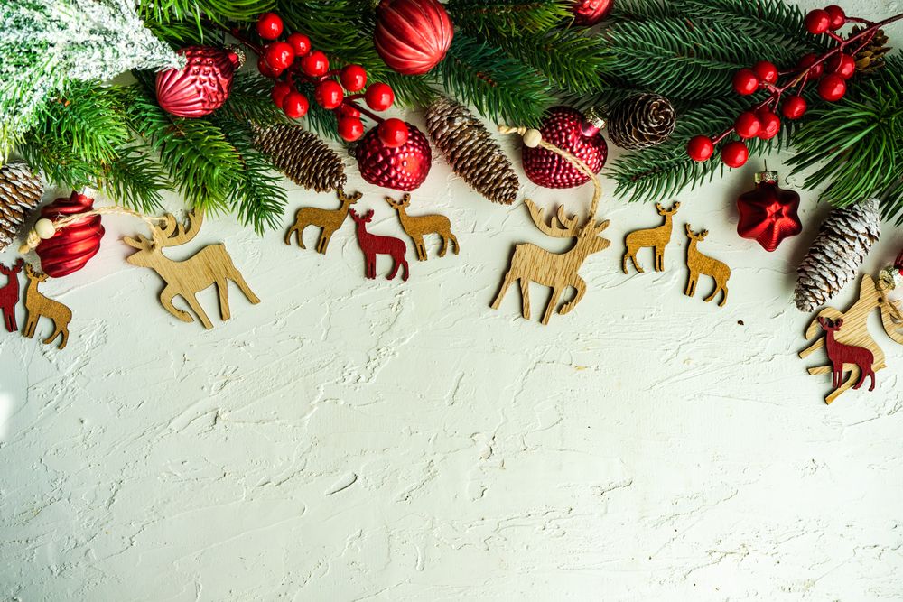 Wintry pine branch, reindeer ornaments and holly berries on top of horizontal frame