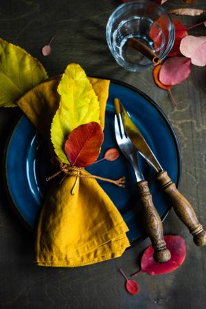 Fall place setting with yellow napkin & colorful leaves on navy plate