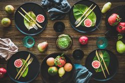 Fresh table setting with leaves on dark plates, with fruit on wooden table