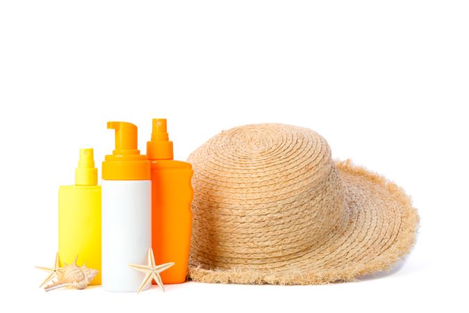 Sunscreen sprays with starfishes and straw hat isolated on plain background. Summer vacation accessories