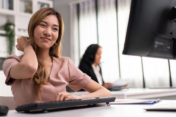 Asian woman sitting in office and holding her sore neck