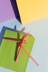 Pink pencils on green book, in space of geometric shapes.