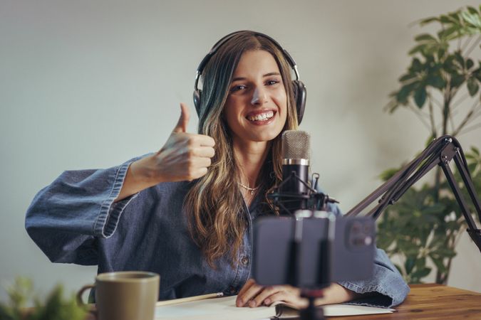 Smiling woman with headphones recording podcast and showing thumbs up gesture