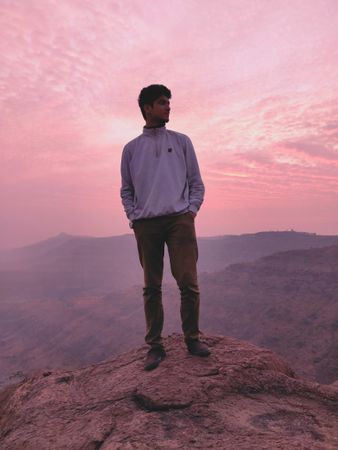 Man standing on rock formation near mountains during sunset