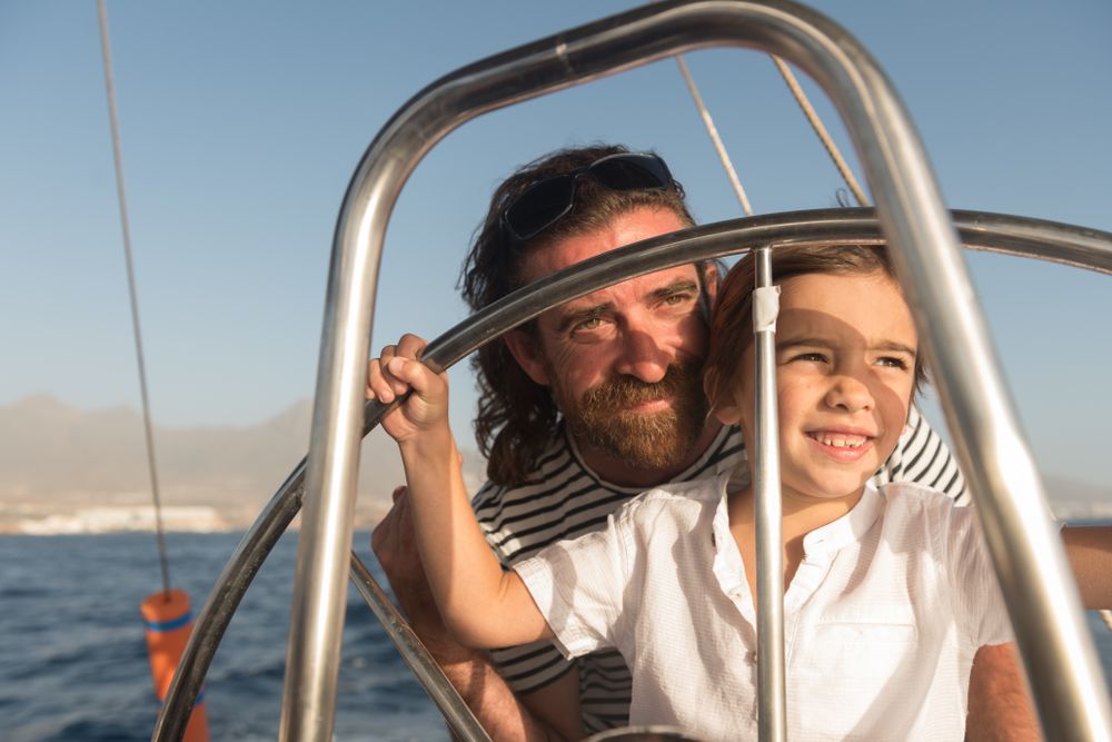 Man with boy holding steering wheel on yacht on water