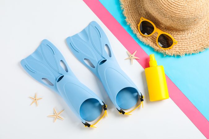 Flippers, sunglasses, straw hat, starfishes and sunscreen on color background