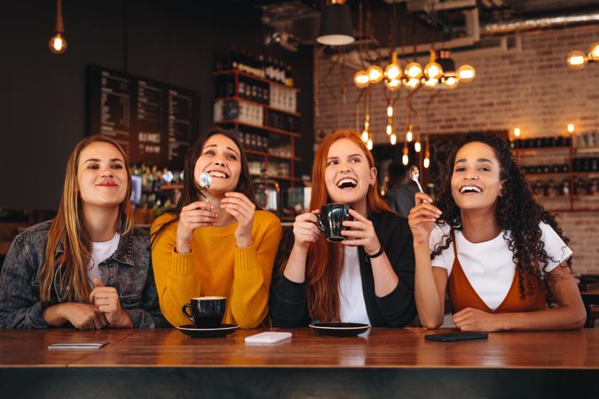 Group of four women sitting at cafe looking away and laughing
