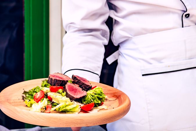 Waiter holding steak salad with fresh lettuce